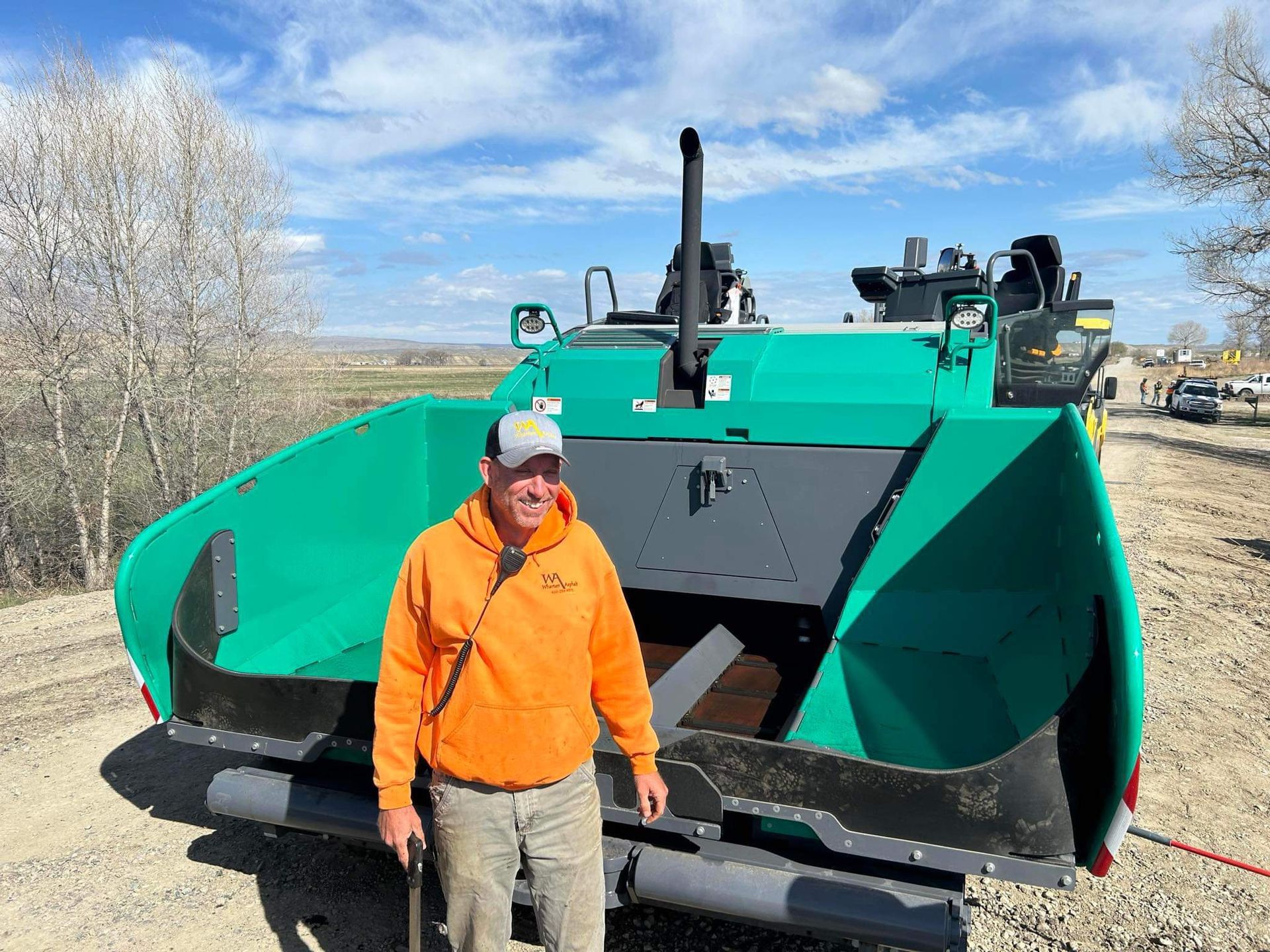 A man in an orange hoodie is standing in front of a green tractor.
