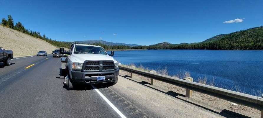A white truck is driving down a highway next to a lake.