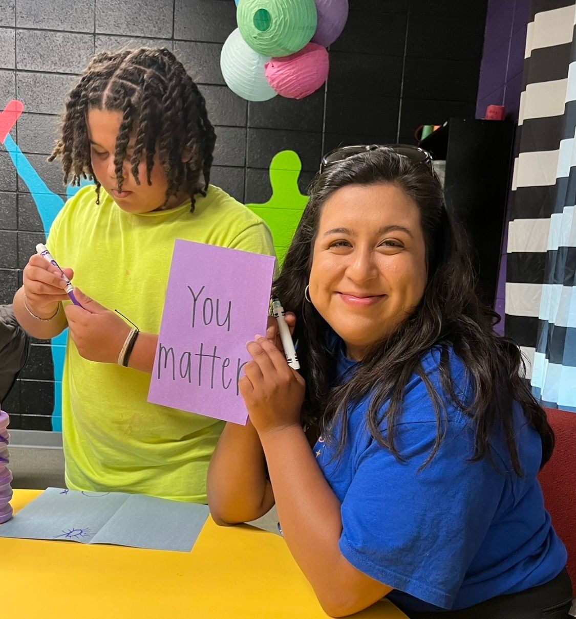 Two people sitting at a table hold a purple sign that says 