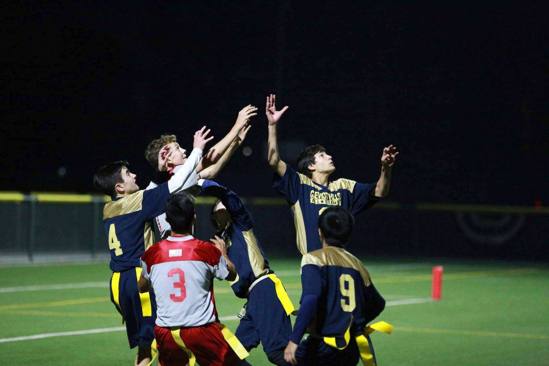 Football player in maroon jersey holding ball, smiling, surrounded by teammates on a field.