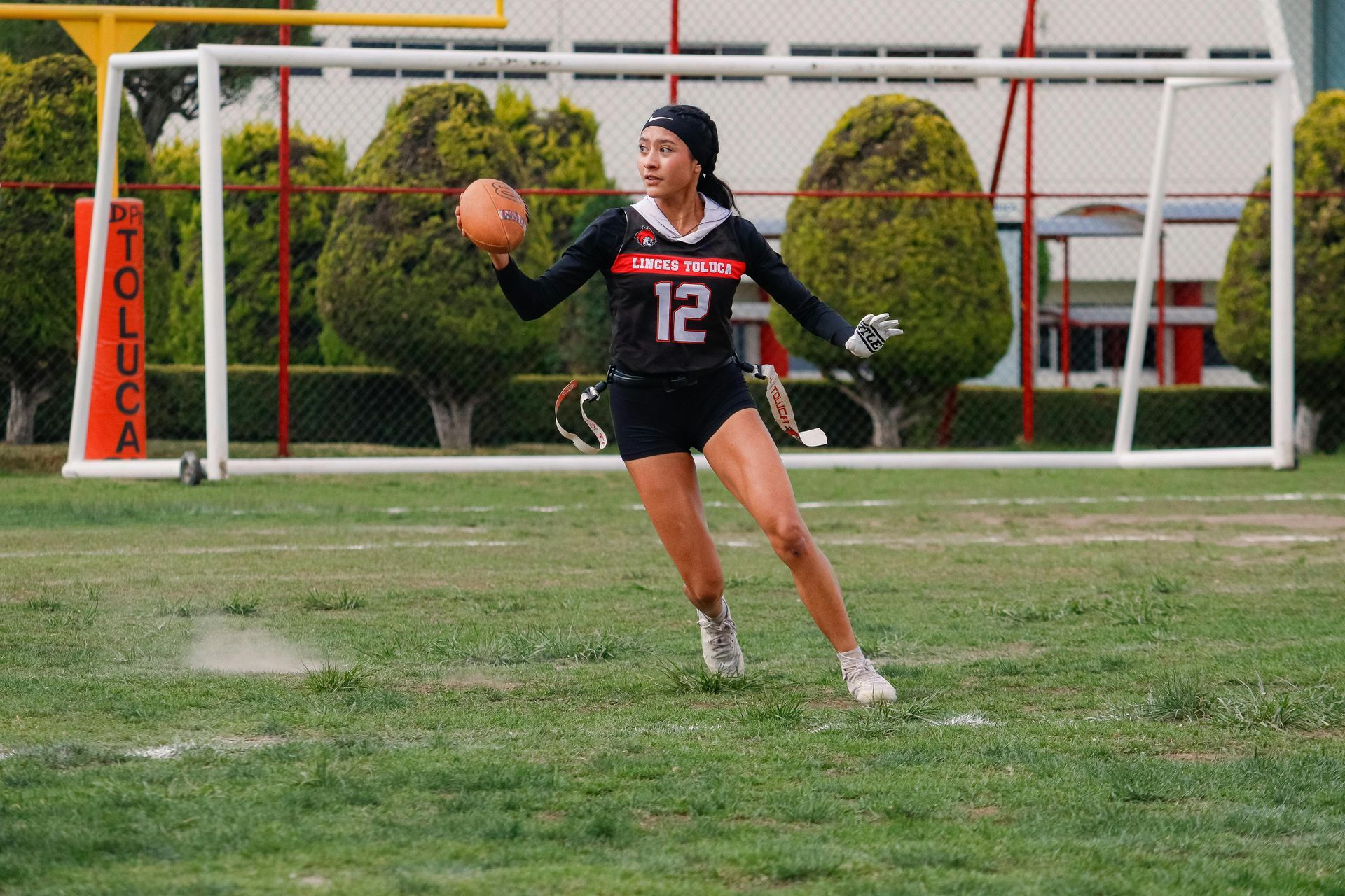 Football players in action on a grassy field; one runs with the ball, pursued by two opponents.
