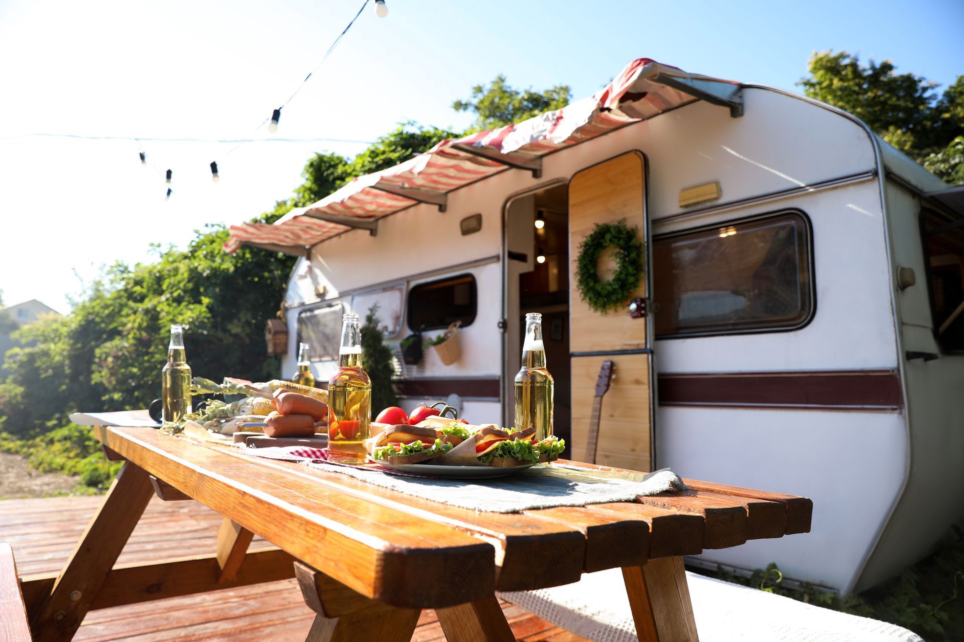 Cozy camper van beside a picnic table set with food, under string lights in a sunny outdoor setting