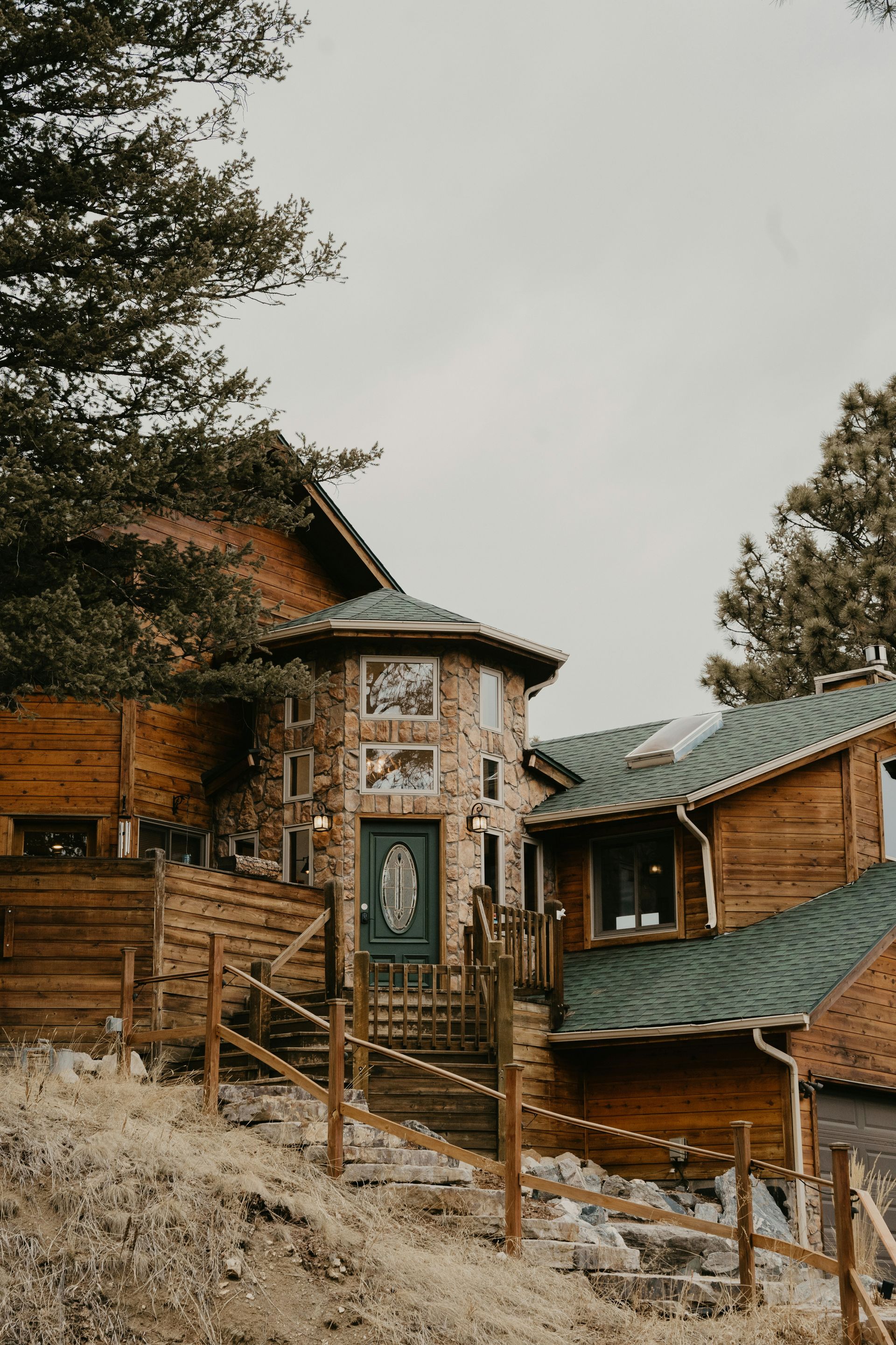 Rustic cabin with stone tower and green door, wooden railings, and a green roof.