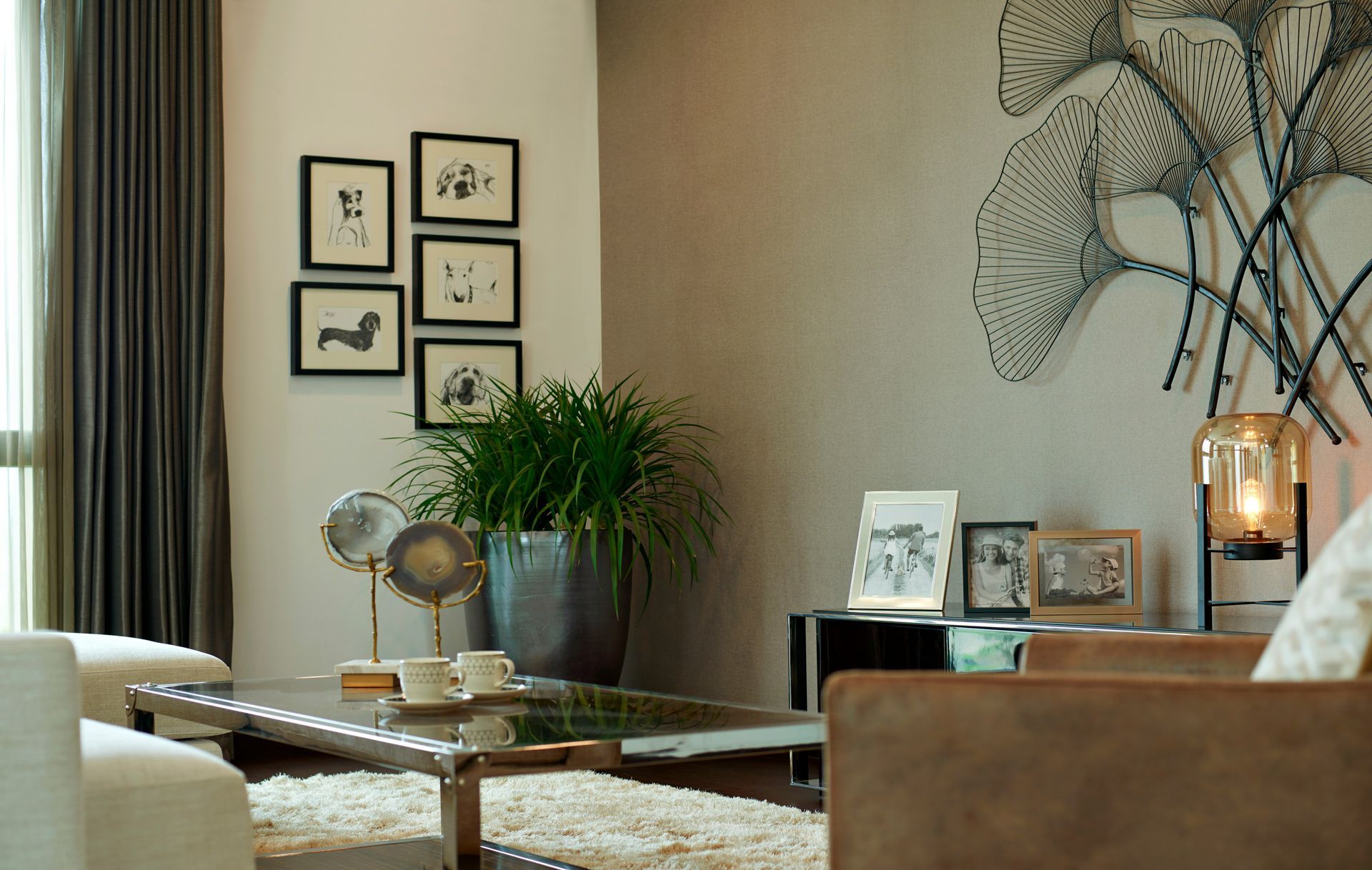 Living room with framed art, plants, coffee table, and neutral-toned furniture; a metal sculpture hangs on the wall.