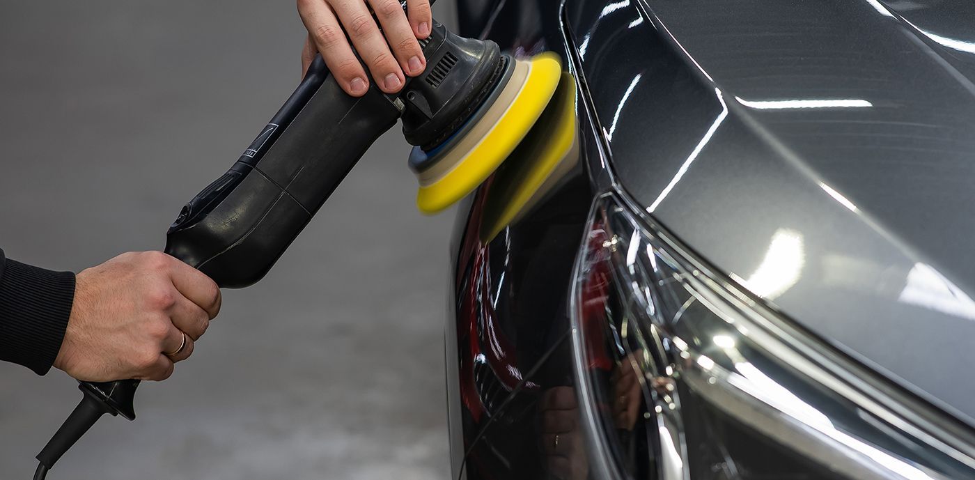 Person using a power buffer to polish the side of a dark car.