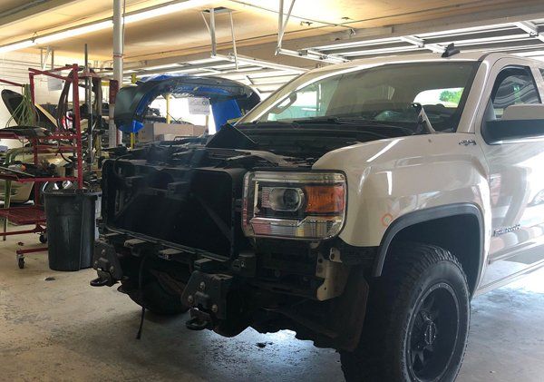 A white truck with the hood up is parked in a garage.