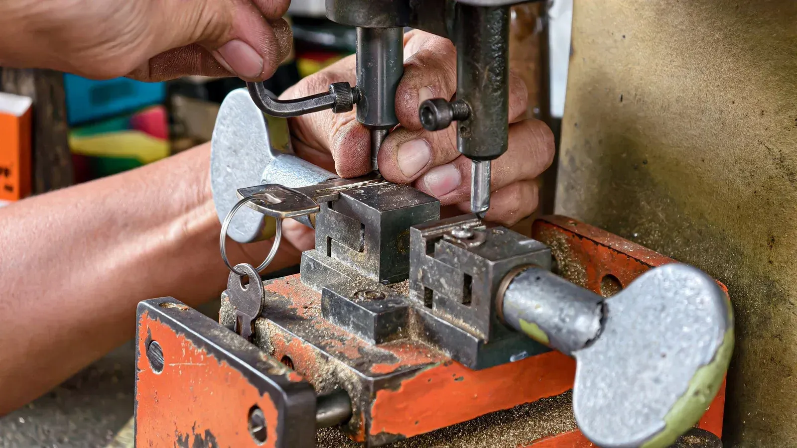 Hands operate a key-cutting machine to duplicate a metal key.