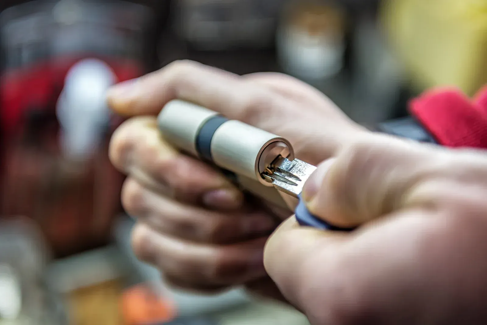 Close-up of hands inserting a key into a metallic door lock cylinder.