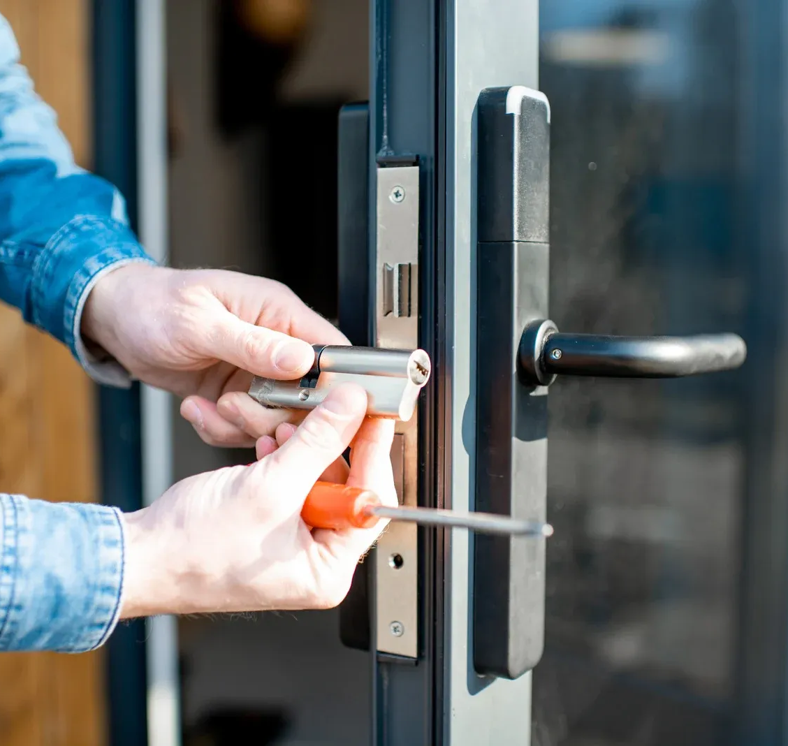A person installing a metal euro profile cylinder lock into a black door handle assembly with a screwdriver.