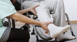 medico massaggia la gamba a un paziente sulla sedia a rotelle