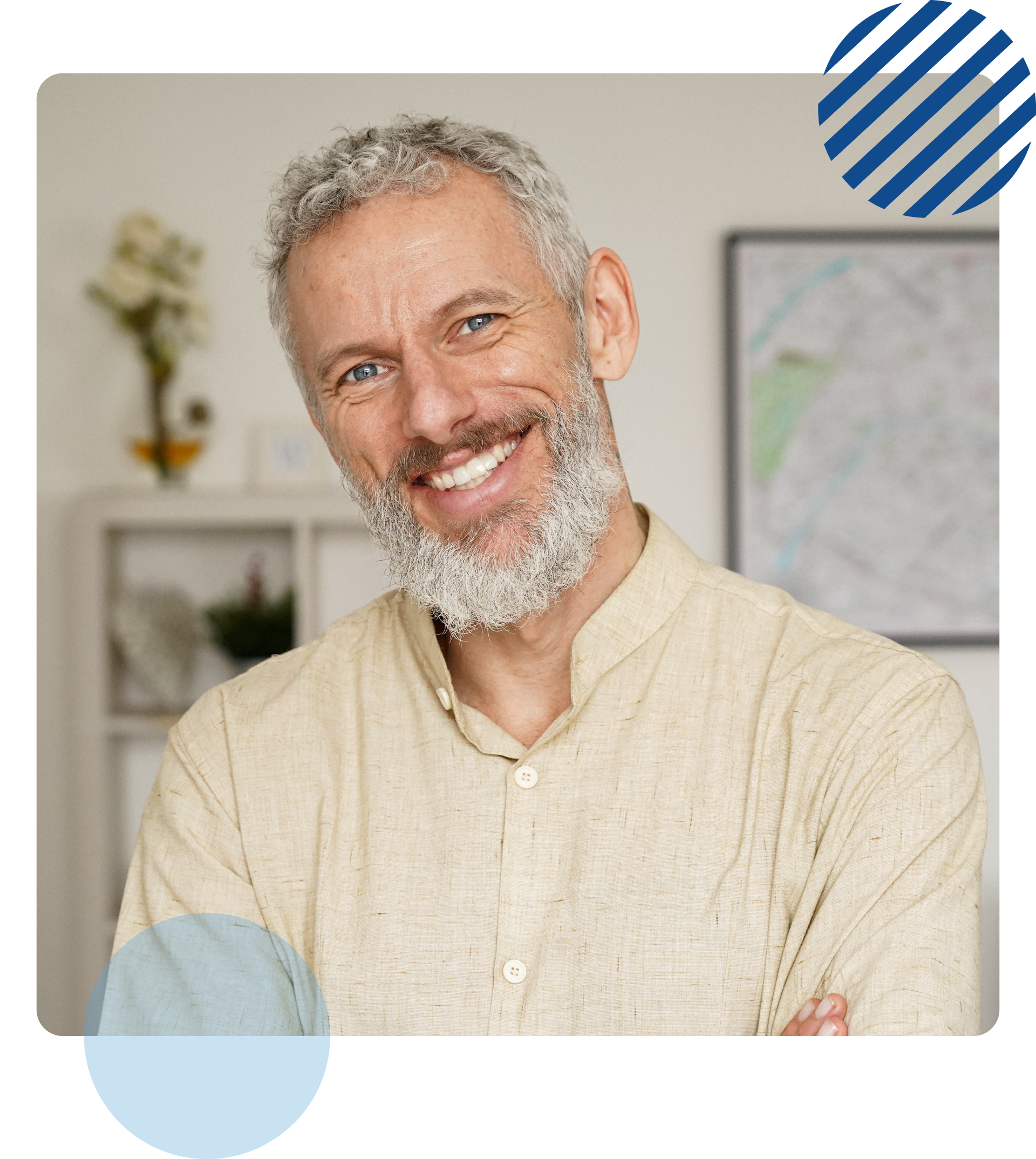 Smiling man with gray beard, tan shirt, arms crossed, indoors.