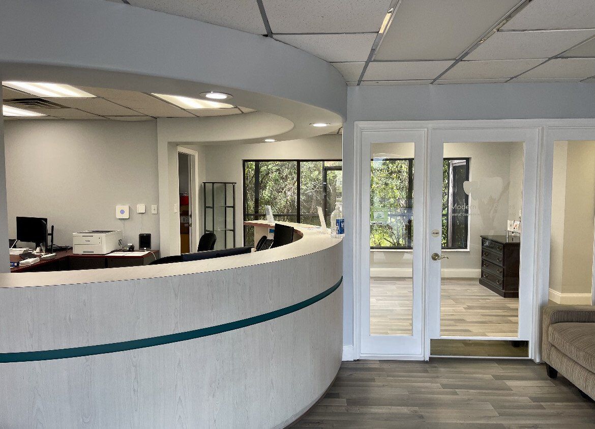Reception area with curved white desk, glass doors, and view of greenery.