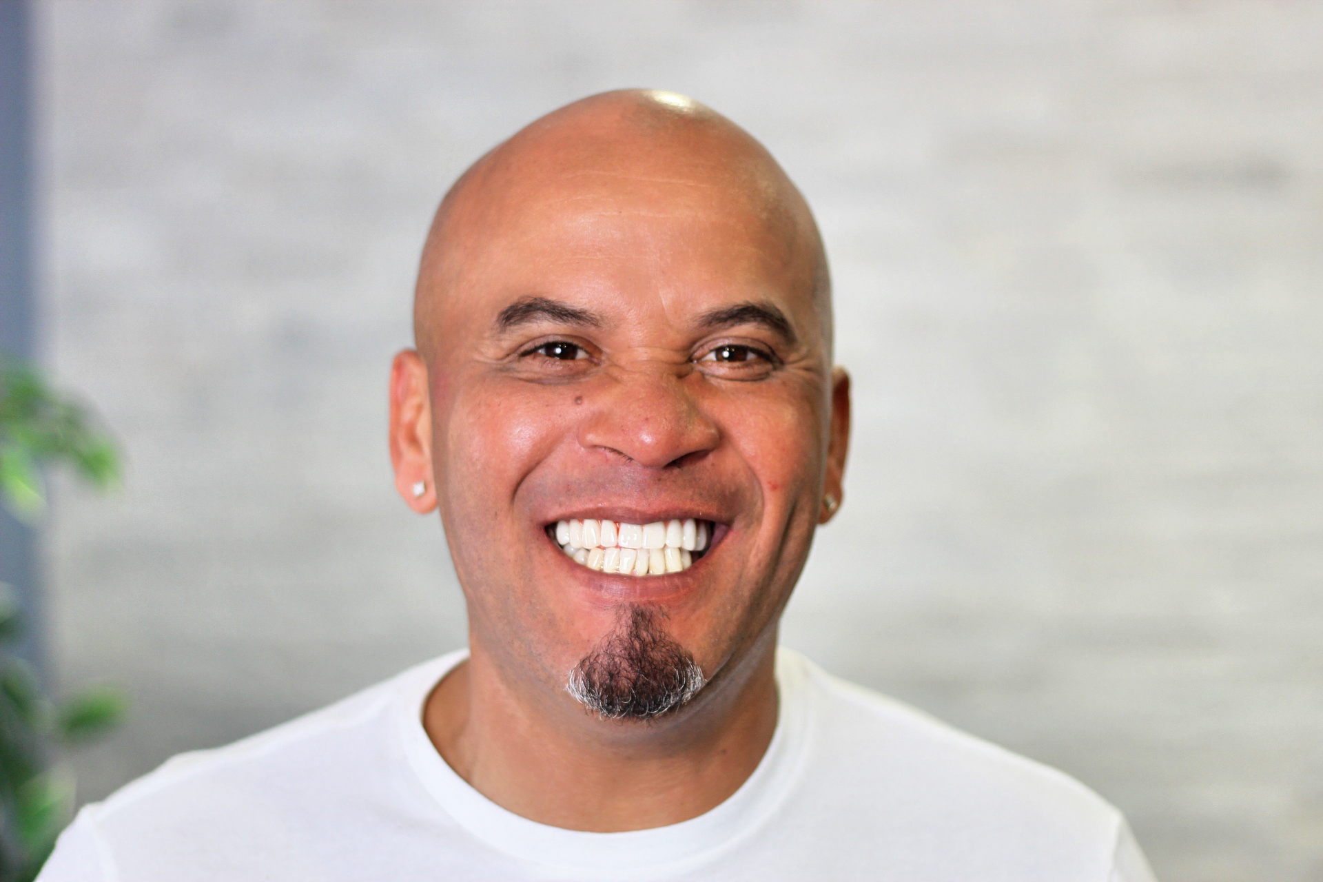 Smiling bald man with a goatee in a white shirt, standing against a blurred light background