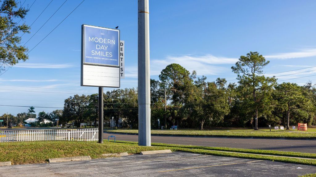 Two women talking at a desk in a bright office, with a sign-in sheet and laptop nearby
