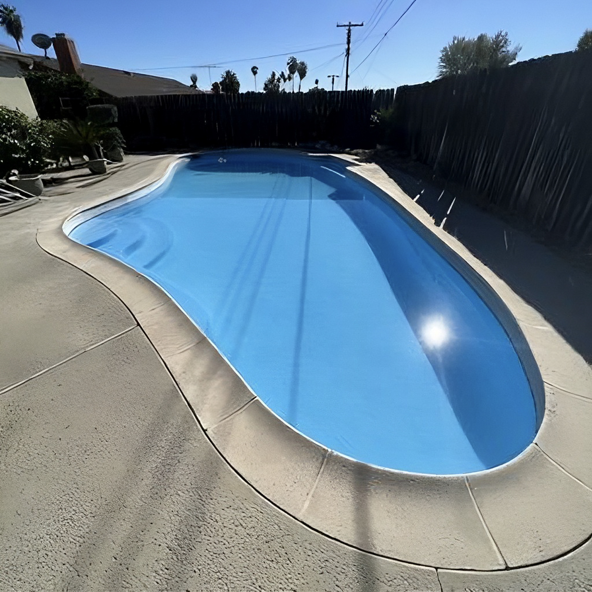 Swimming pool with blue water and concrete patio, bordered by a black fence.