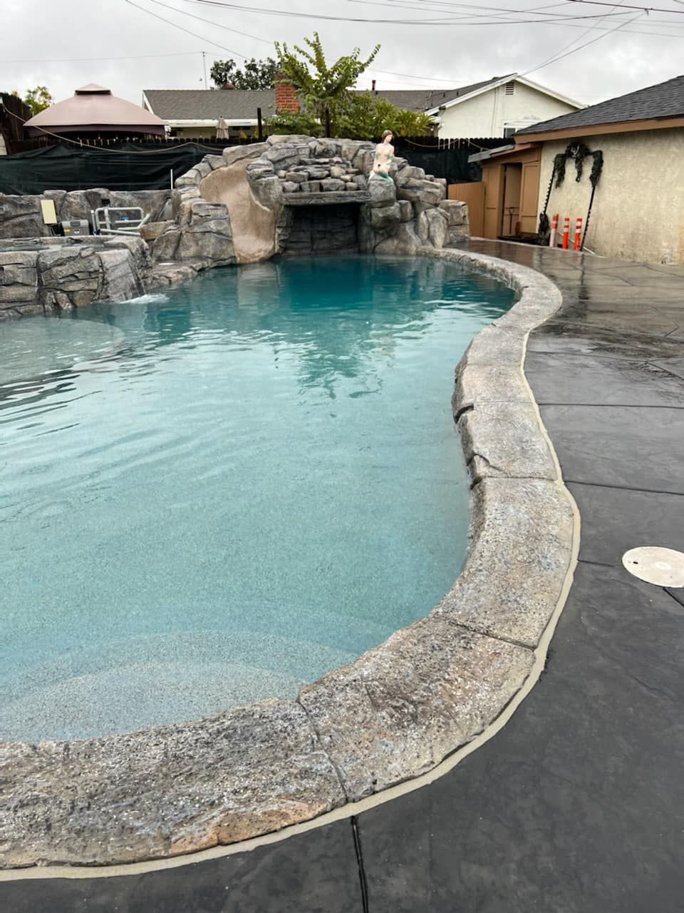 Pool with rock waterfall feature; water is turquoise, surrounded by gray concrete.