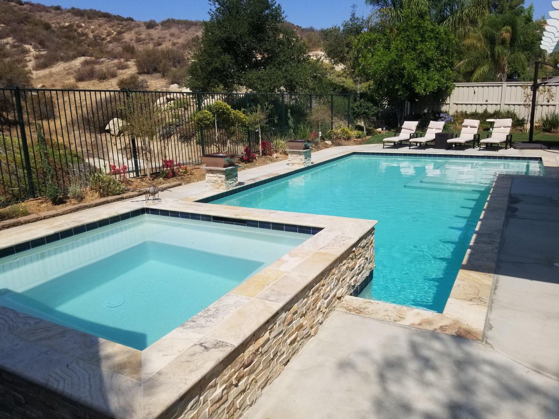 Pool and spa with turquoise water surrounded by a stone deck, with lounge chairs in the background.