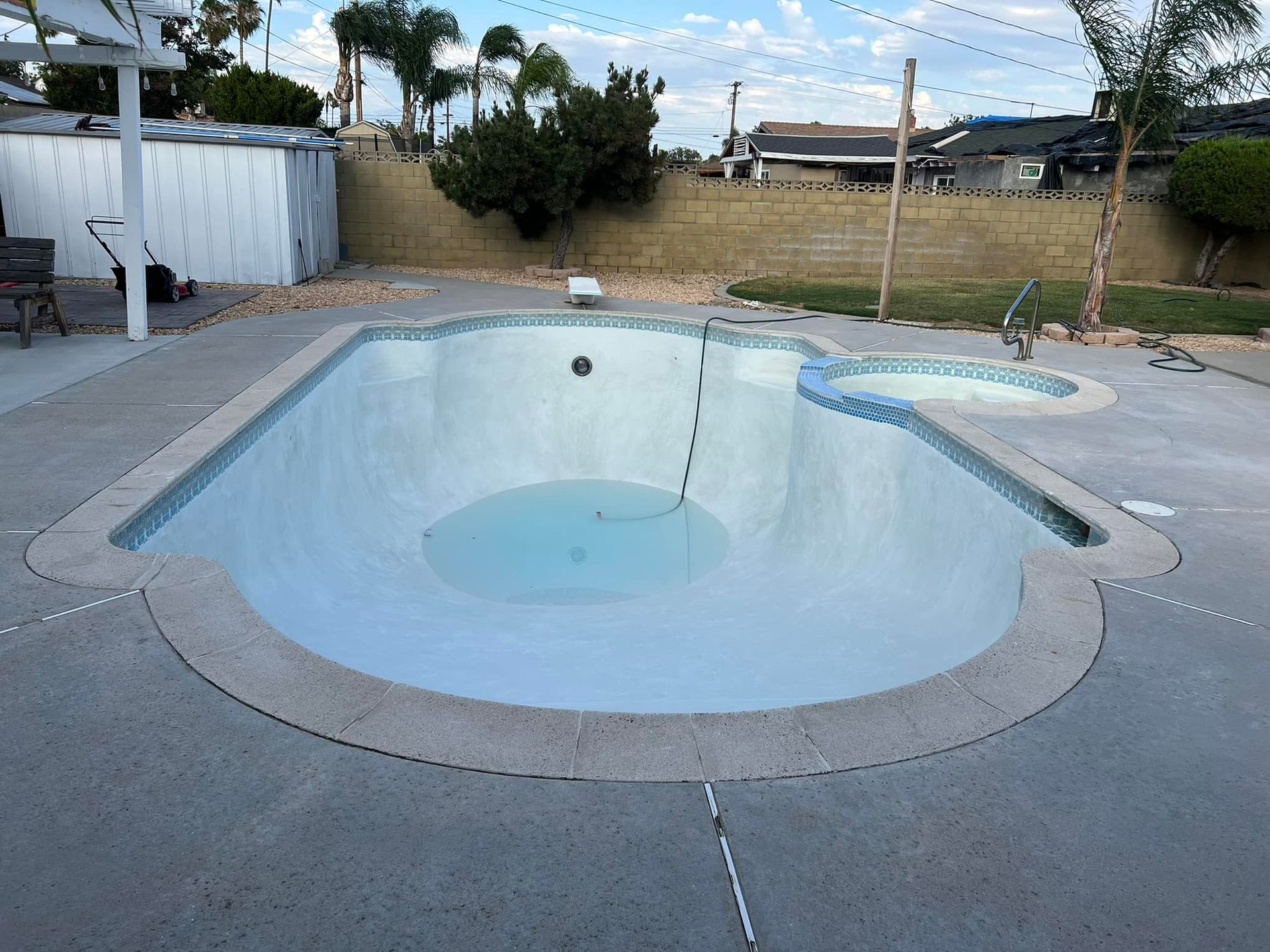 Empty swimming pool with curved edges, surrounded by concrete patio. A spa is adjacent.