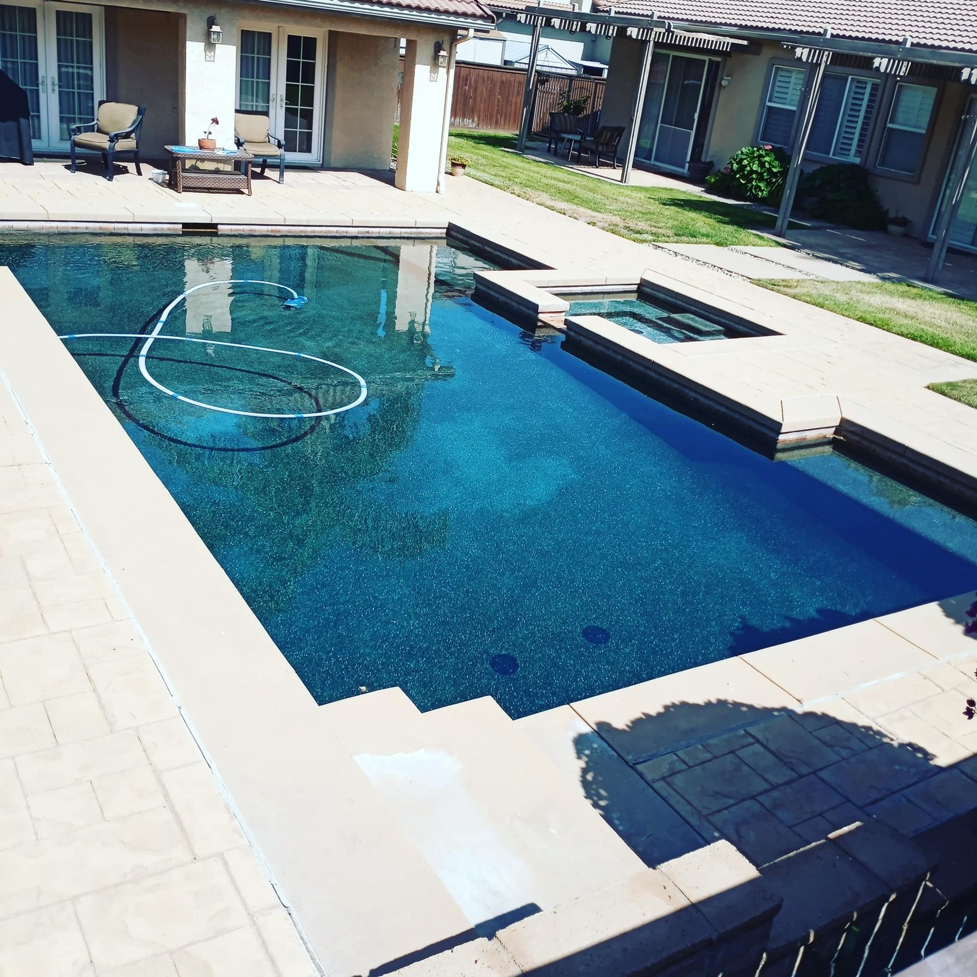 A rectangular blue swimming pool with attached spa, surrounded by stone patio.