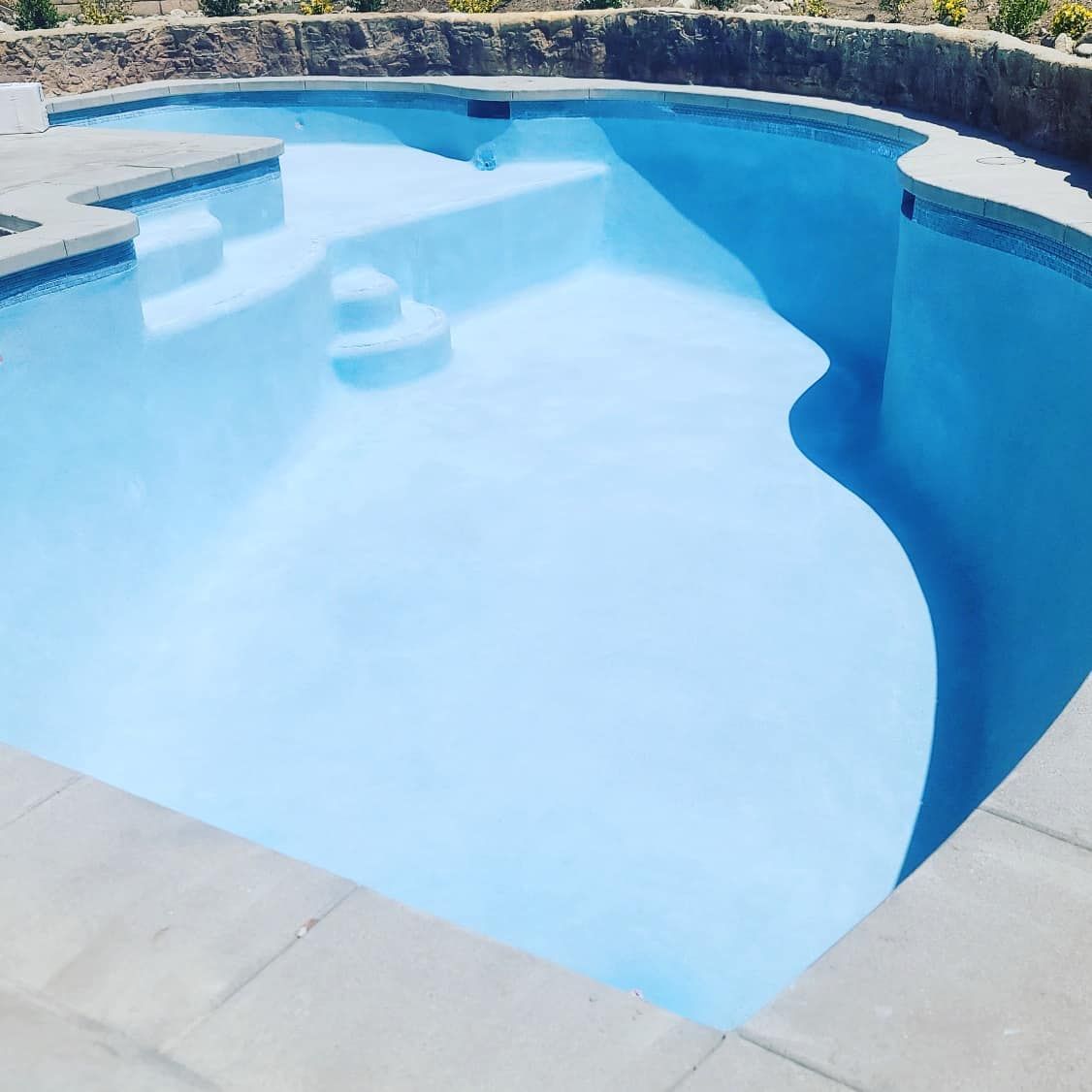 Blue-tiled swimming pool with a unique curved design, surrounded by stone coping and a rock retaining wall.
