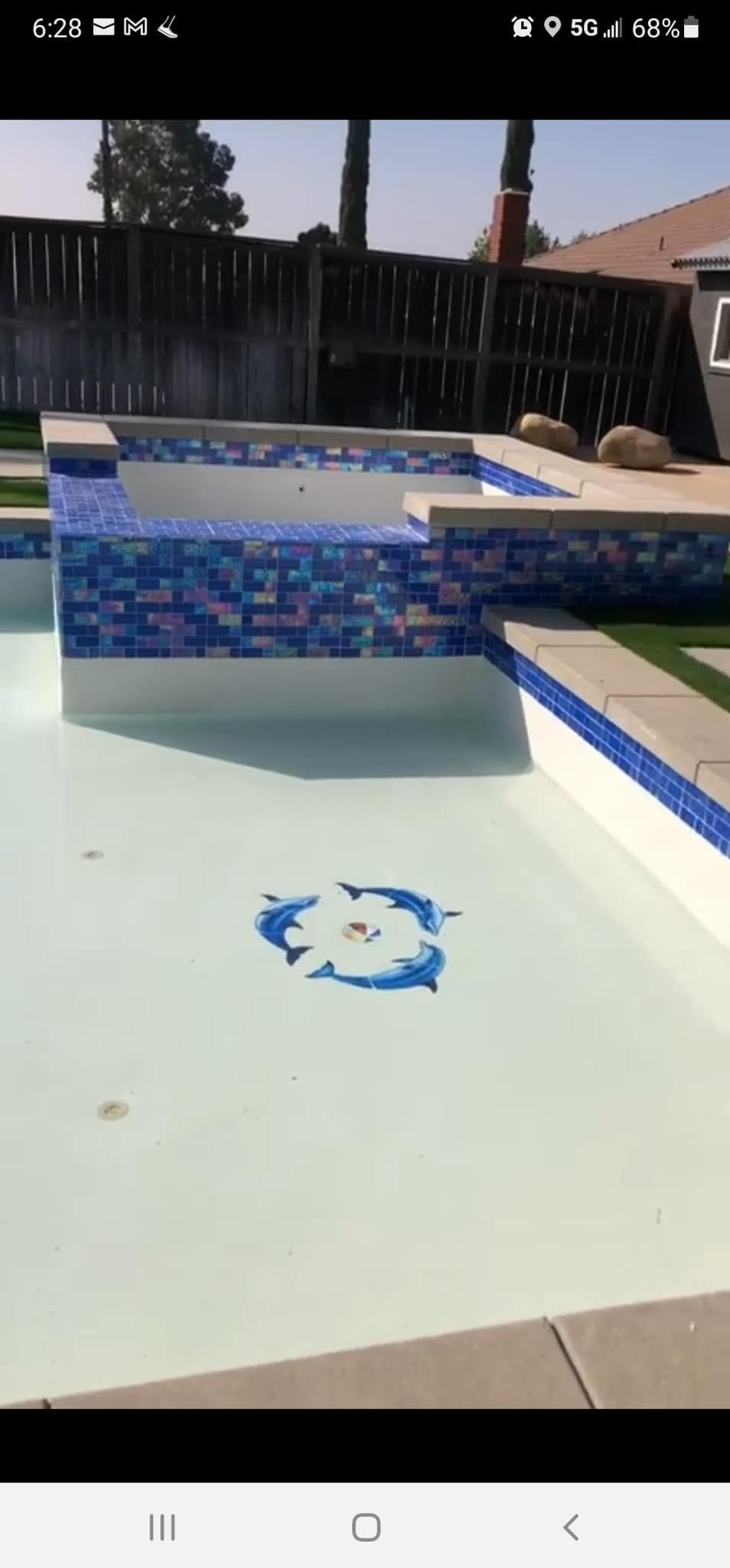 A pool with blue mosaic tile and a dolphin mosaic on the pool floor.