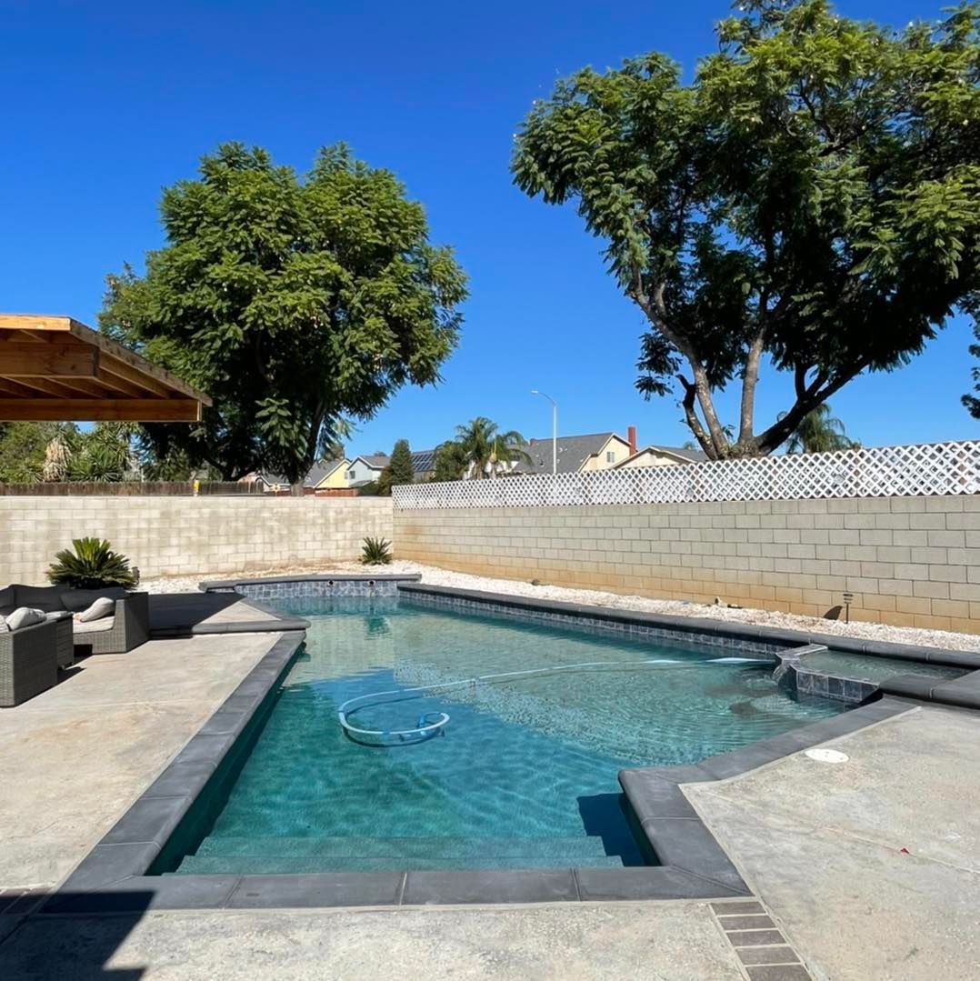 Pool with turquoise water surrounded by a concrete patio and a stone wall under a bright blue sky.