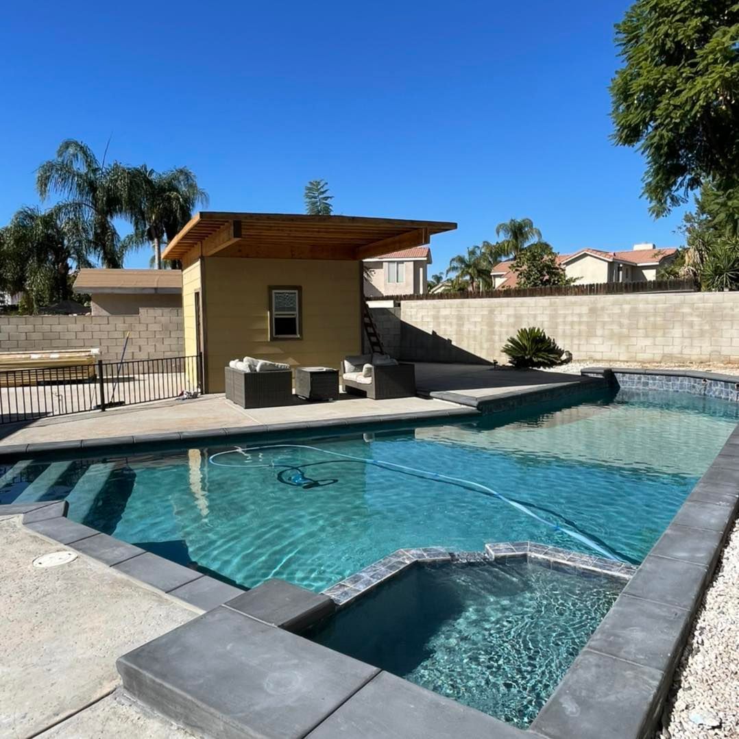 Backyard pool with spa, lounge area, and yellow cabana under a blue sky.