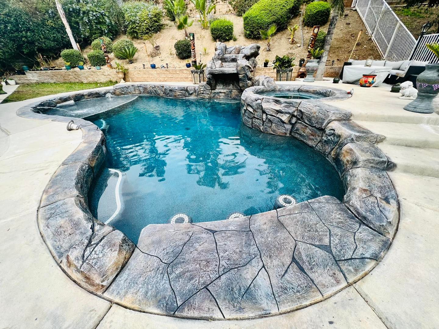 Backyard pool with rock waterfall and surrounding stone border.
