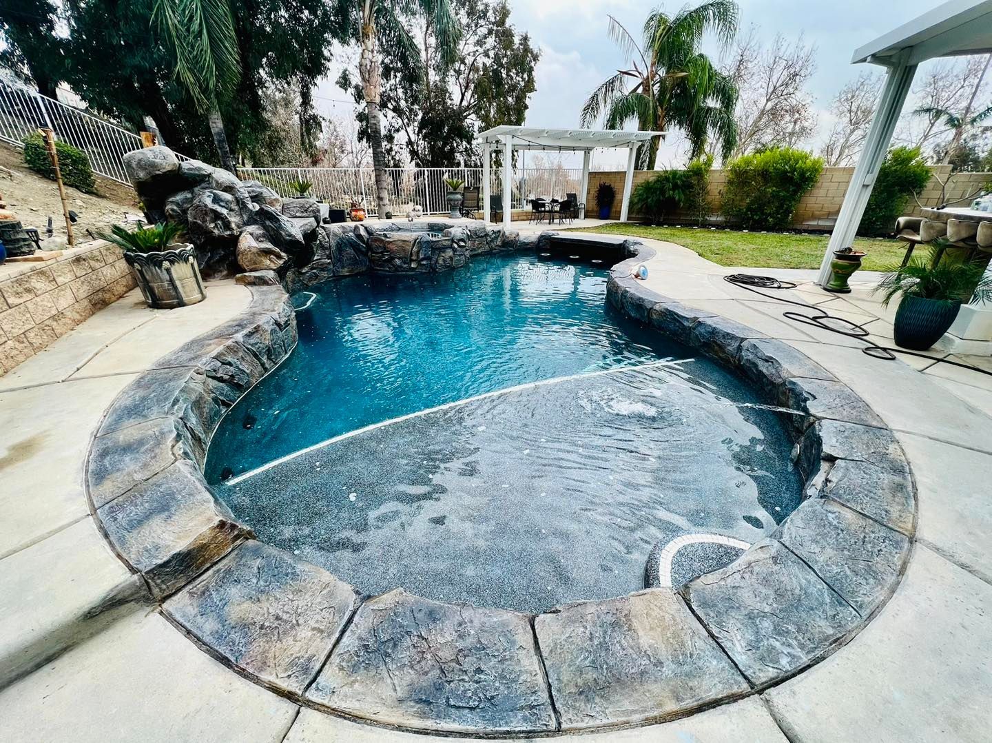 A dark blue swimming pool with stone trim and rock feature, set in a backyard.