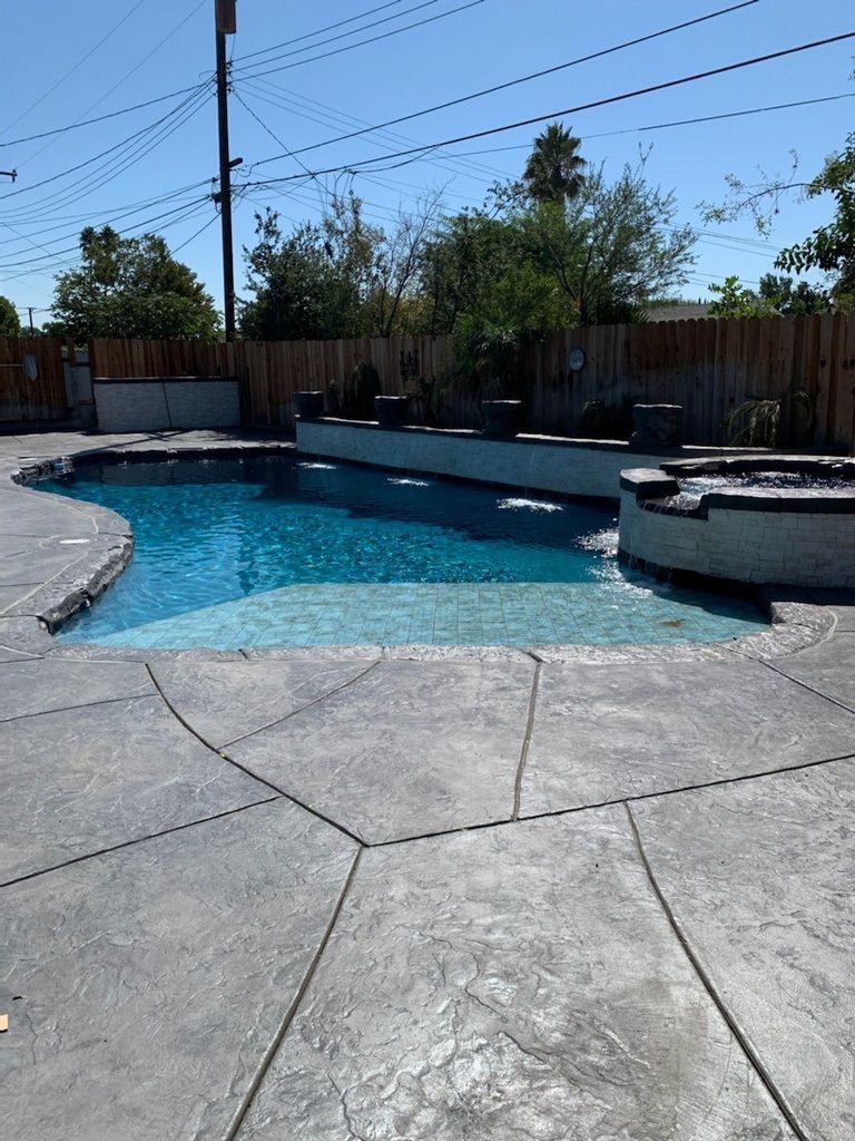 Swimming pool with gray stamped concrete, blue water, and a wooden fence.