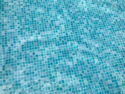 Aqua blue swimming pool with tiled floor reflecting sunlight.