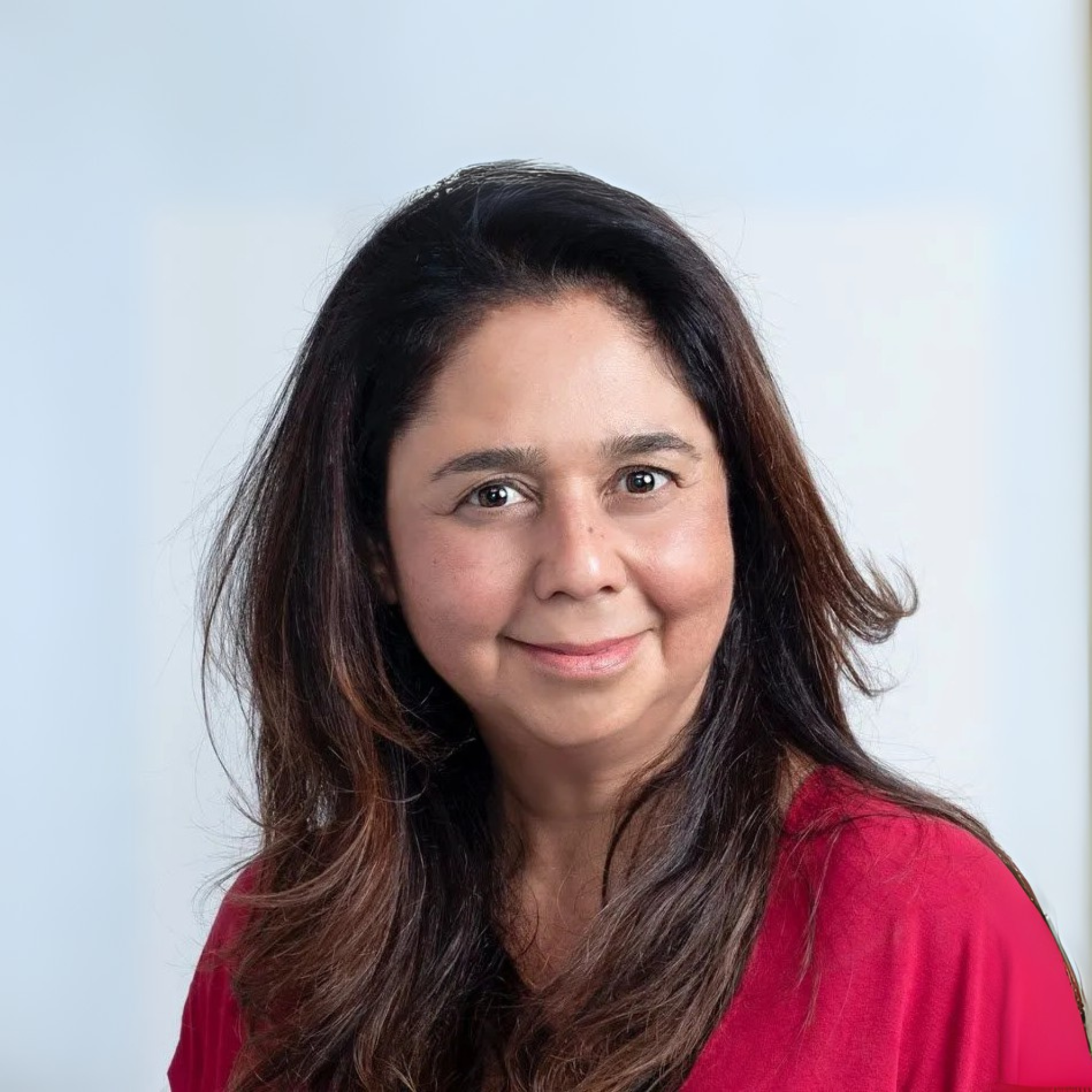 Woman with long dark hair smiles, wearing a red shirt, against a white background.