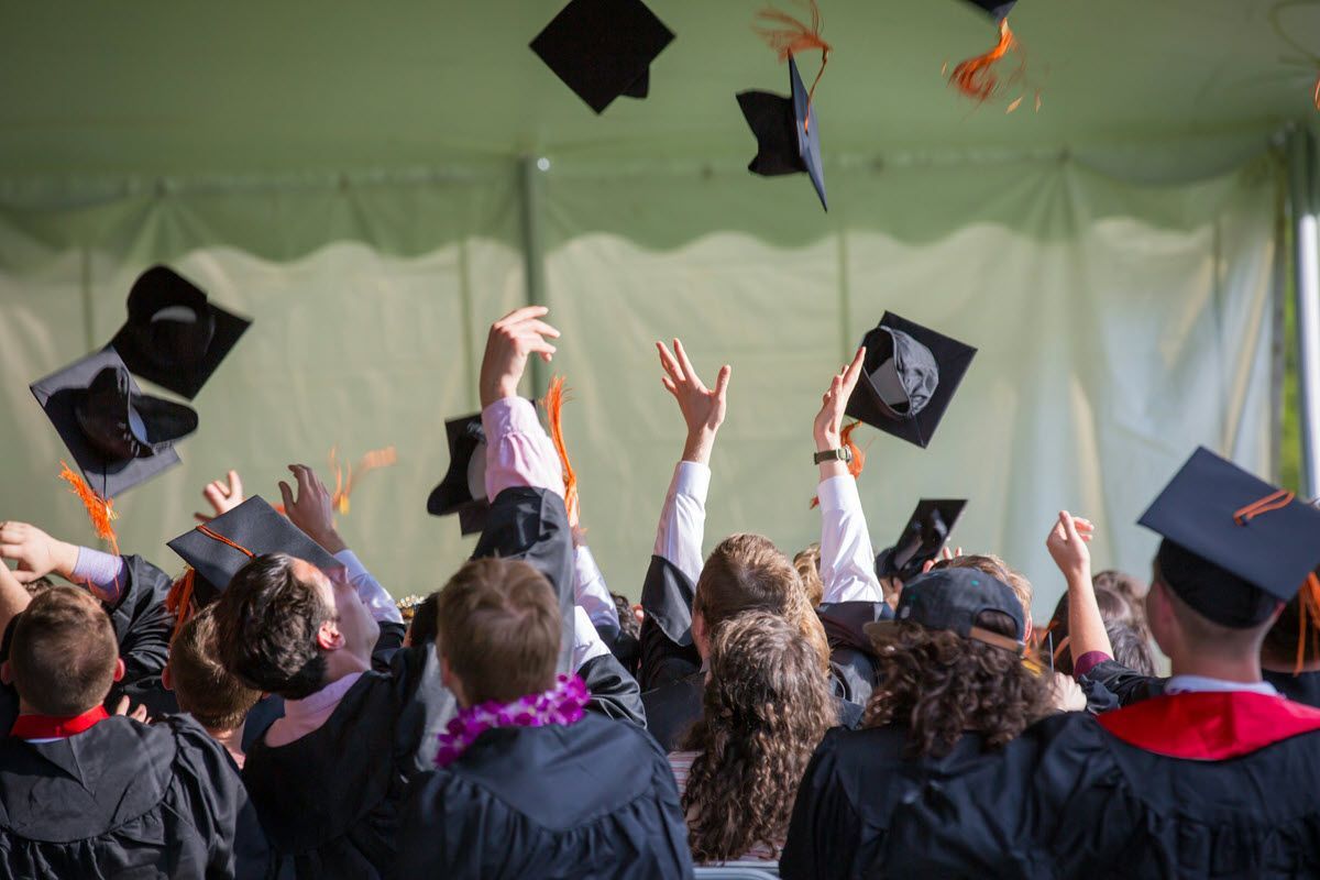 Graduates in black gowns toss mortarboards in the air, orange tassels visible.