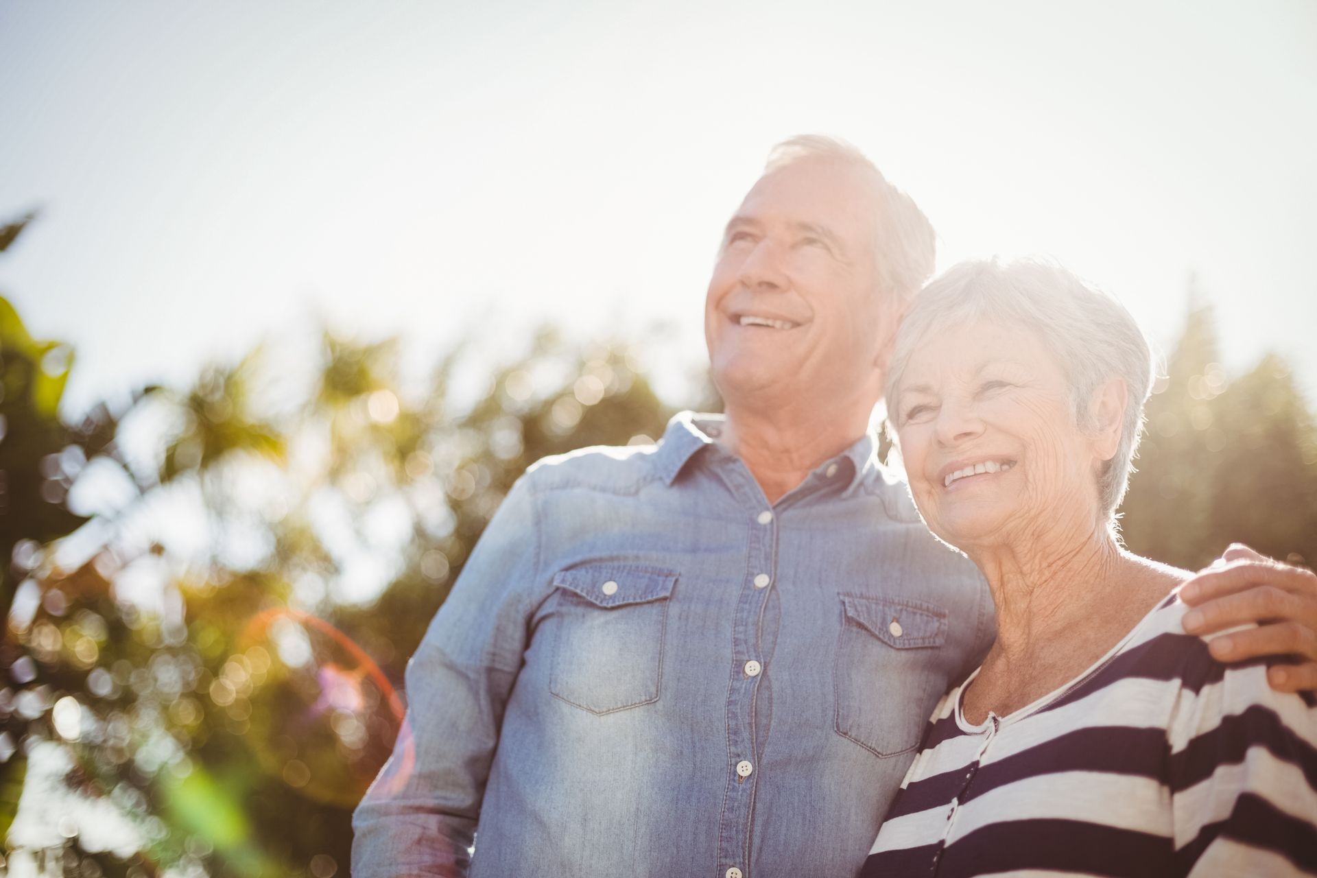 Smiling older couple embracing outdoors in sunlight.