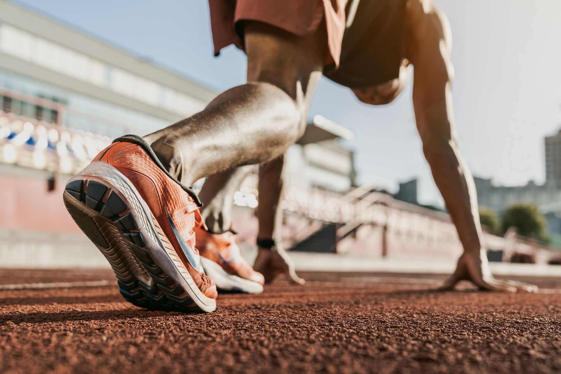Athlete in starting position on a red track, hands down, orange and black shoes.