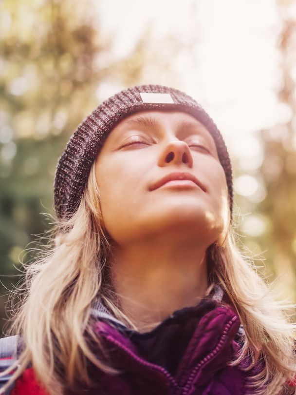 Woman with eyes closed, sunlight, beanie outdoors.