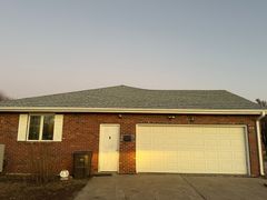 Brick house with white garage door, small window, and icy roof. Evening light reflects on garage.