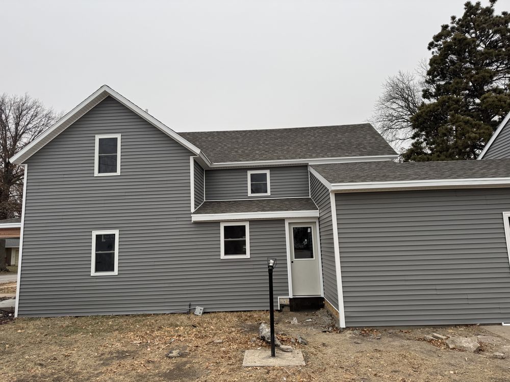 Gray house with vinyl siding and white trim under a cloudy sky.