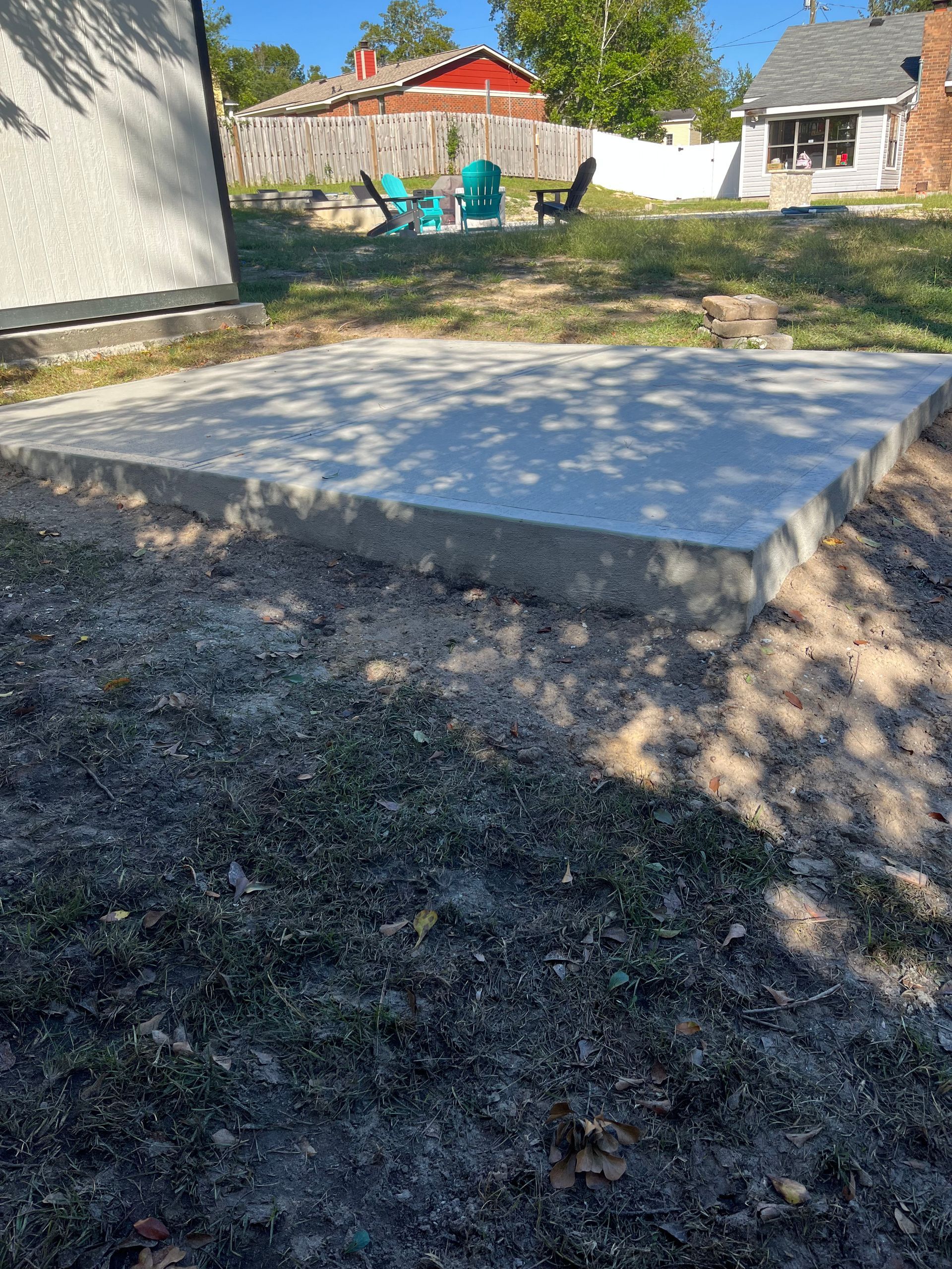 Concrete slab in a yard, surrounded by grass and dirt. A few chairs are in the background.