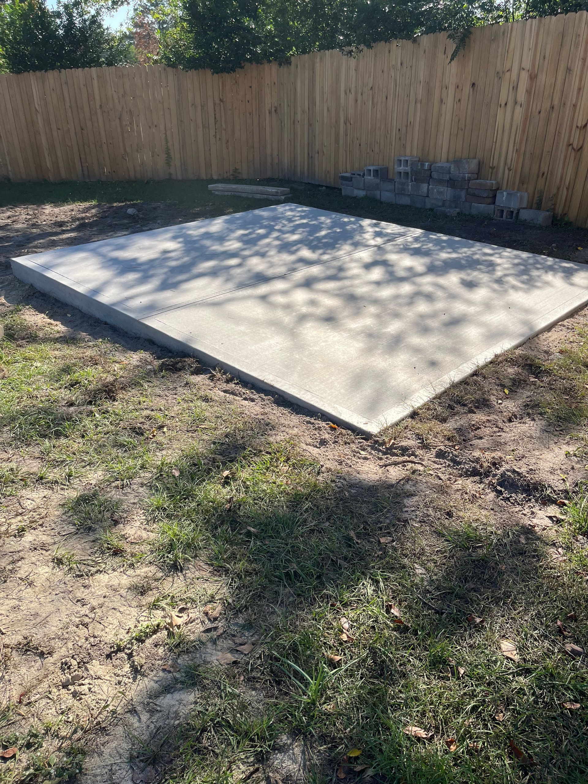 Concrete patio in a grassy backyard with a wooden fence.