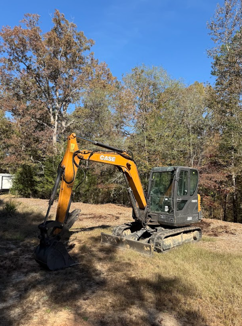 Yellow and black Case excavator on a grassy area with trees and a clear blue sky.