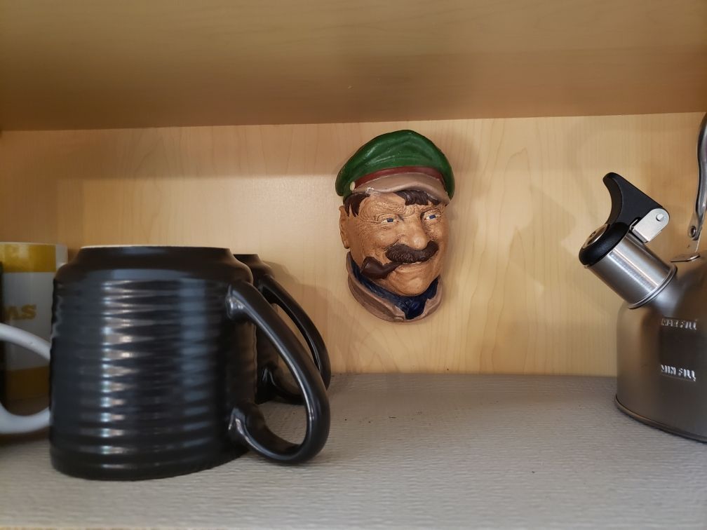 A shelf with a coffee mug, a Mario head figurine, and a kettle.
