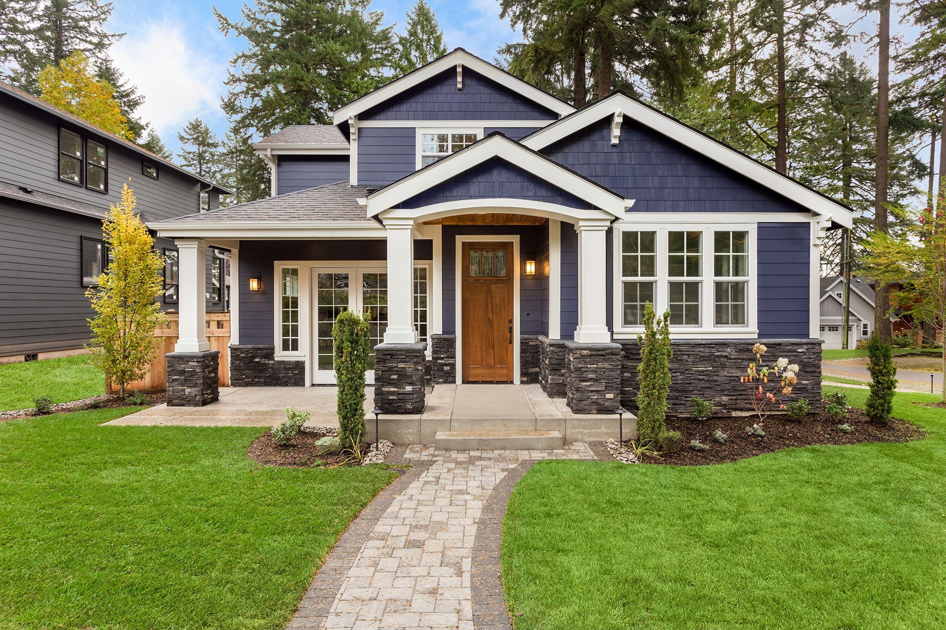 Blue house with white trim and a stone walkway, surrounded by green lawn and trees.