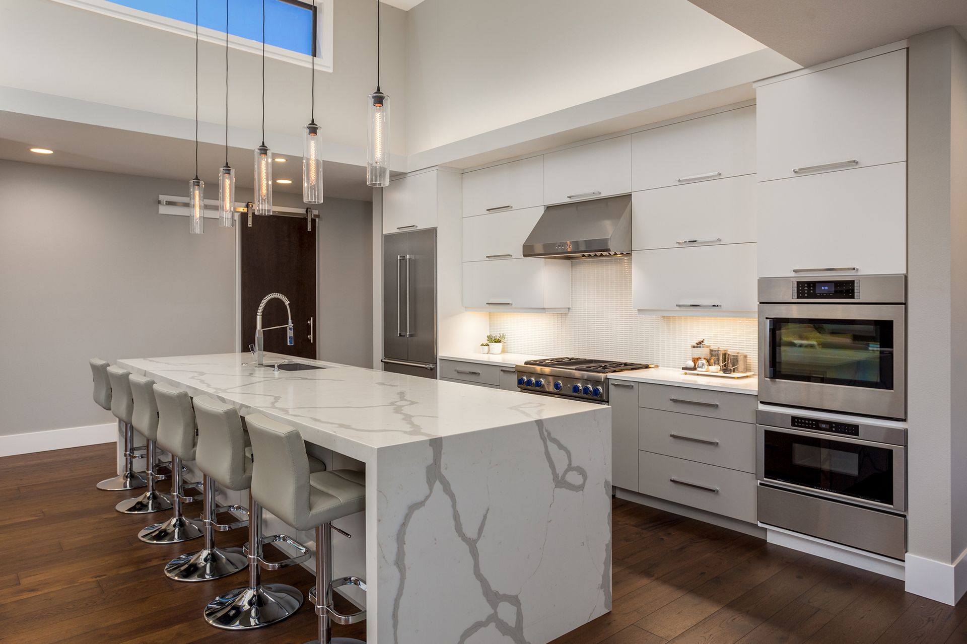 Modern kitchen with a large island with seating, white cabinets, stainless steel appliances, and a skylight.
