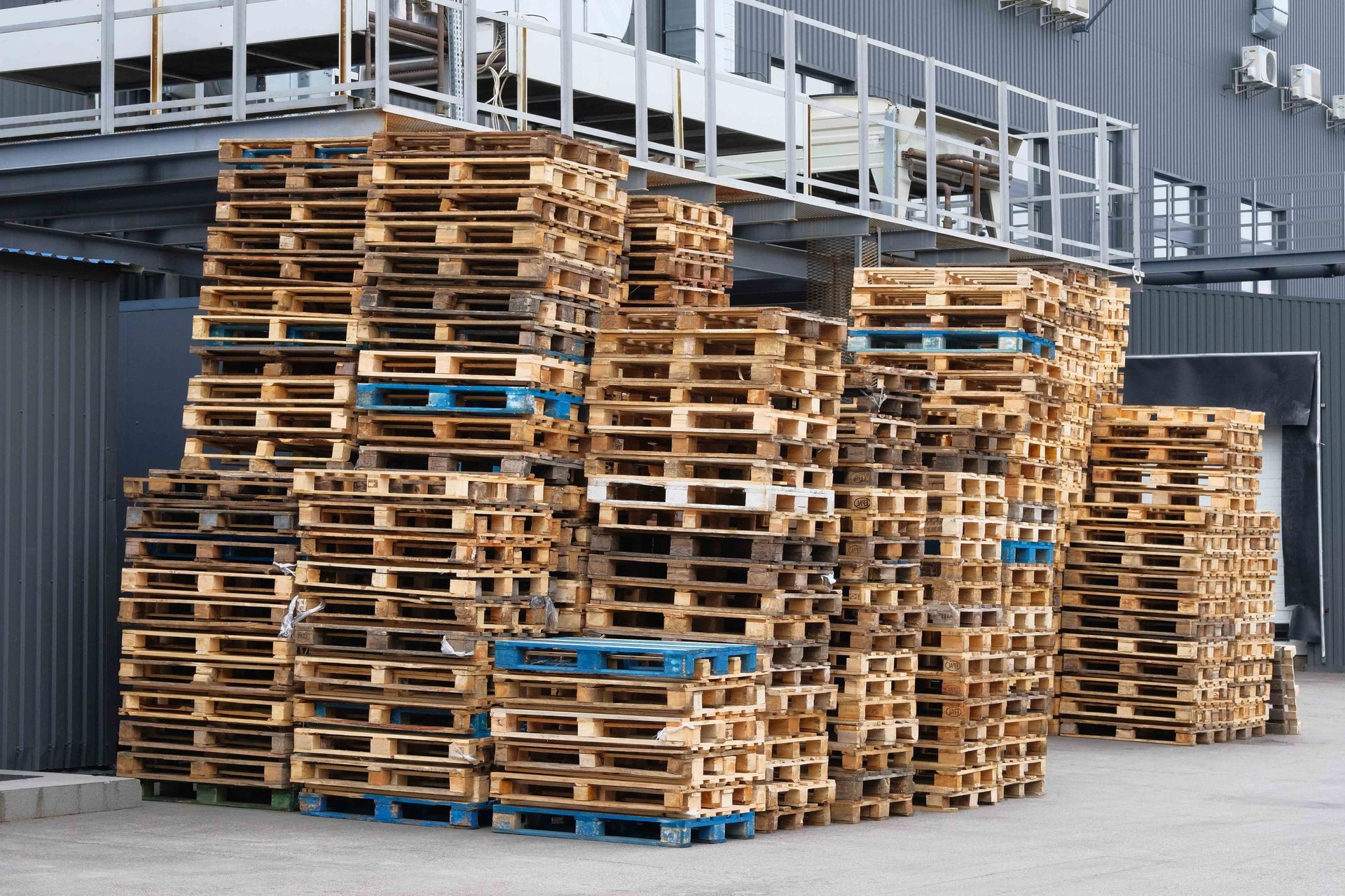 Stacks of wooden shipping pallets stored in an industrial warehouse yard for logistics and freight use.