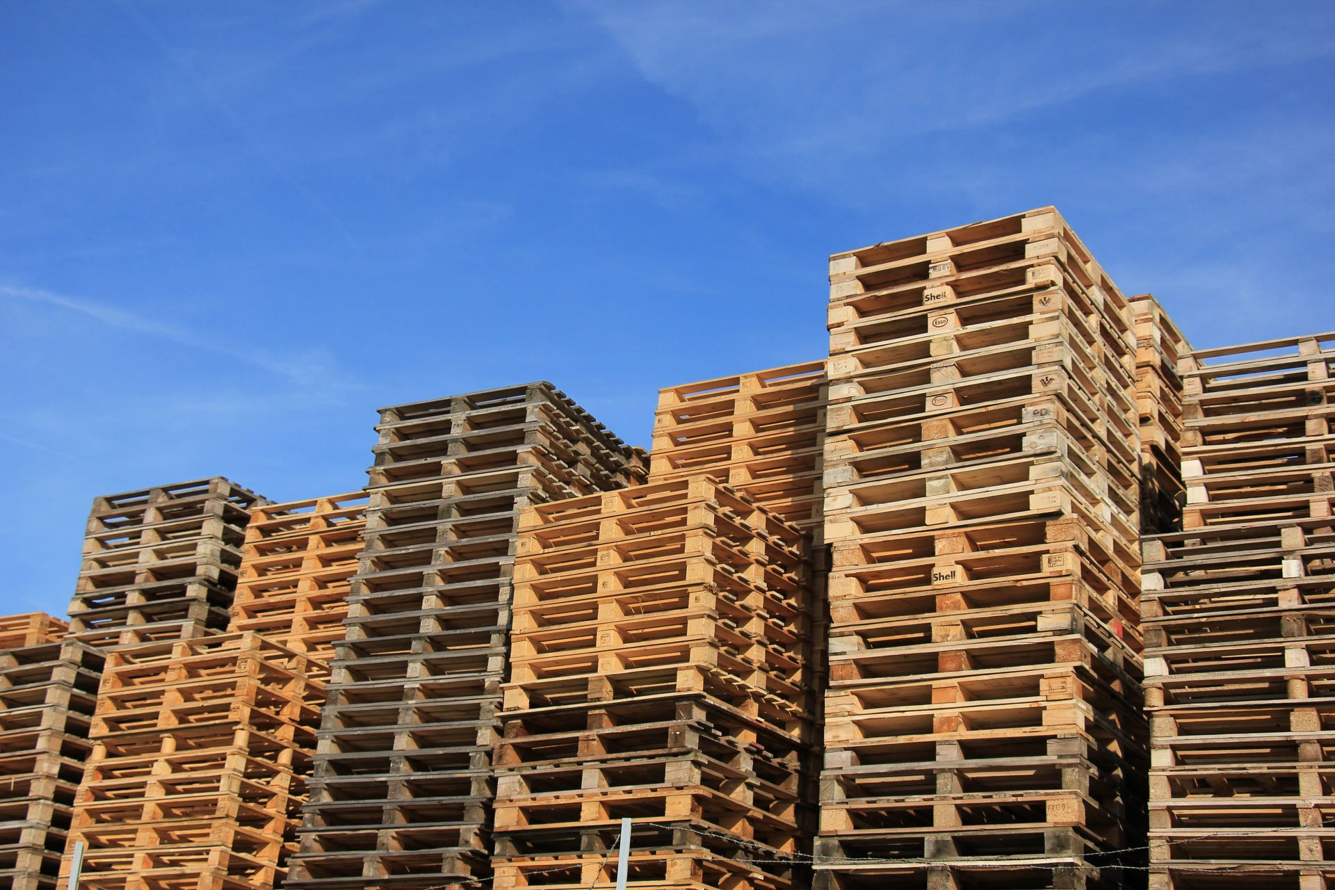 Large stacks of wooden pallets arranged outdoors against a clear blue sky.