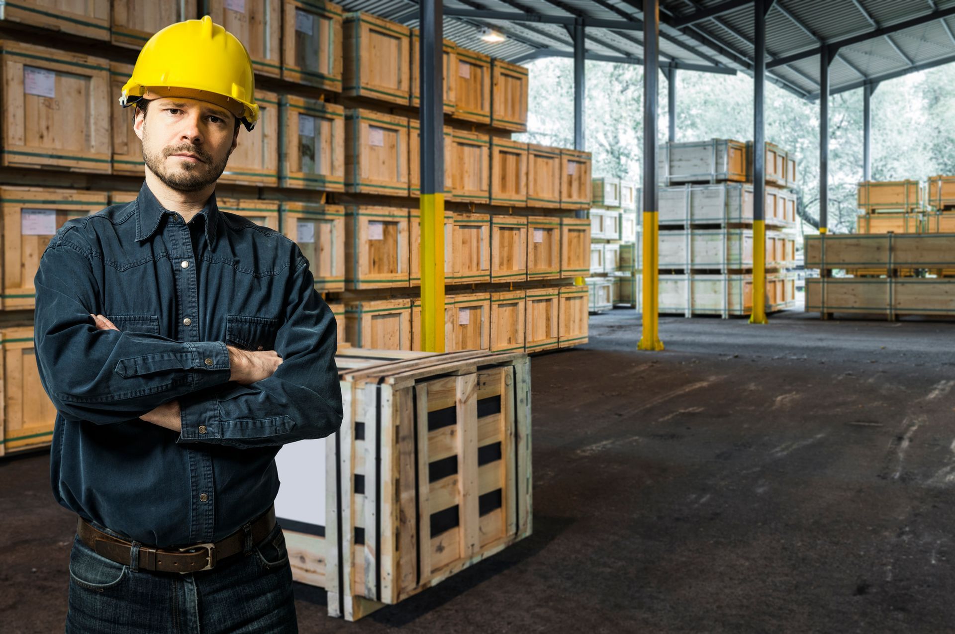 A worker is standing with a wooden crate behind him and rows of crates in the background.