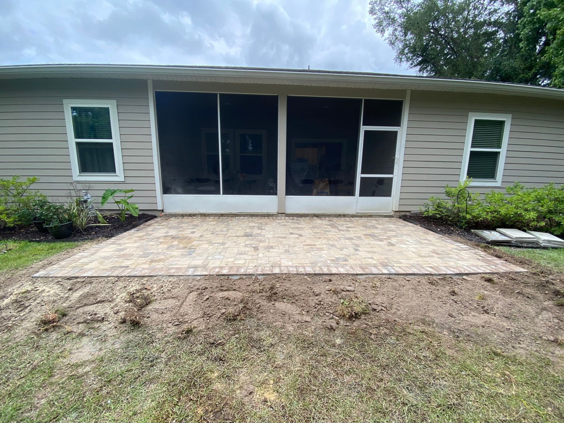 A house with a screened in porch and a patio in front of it.