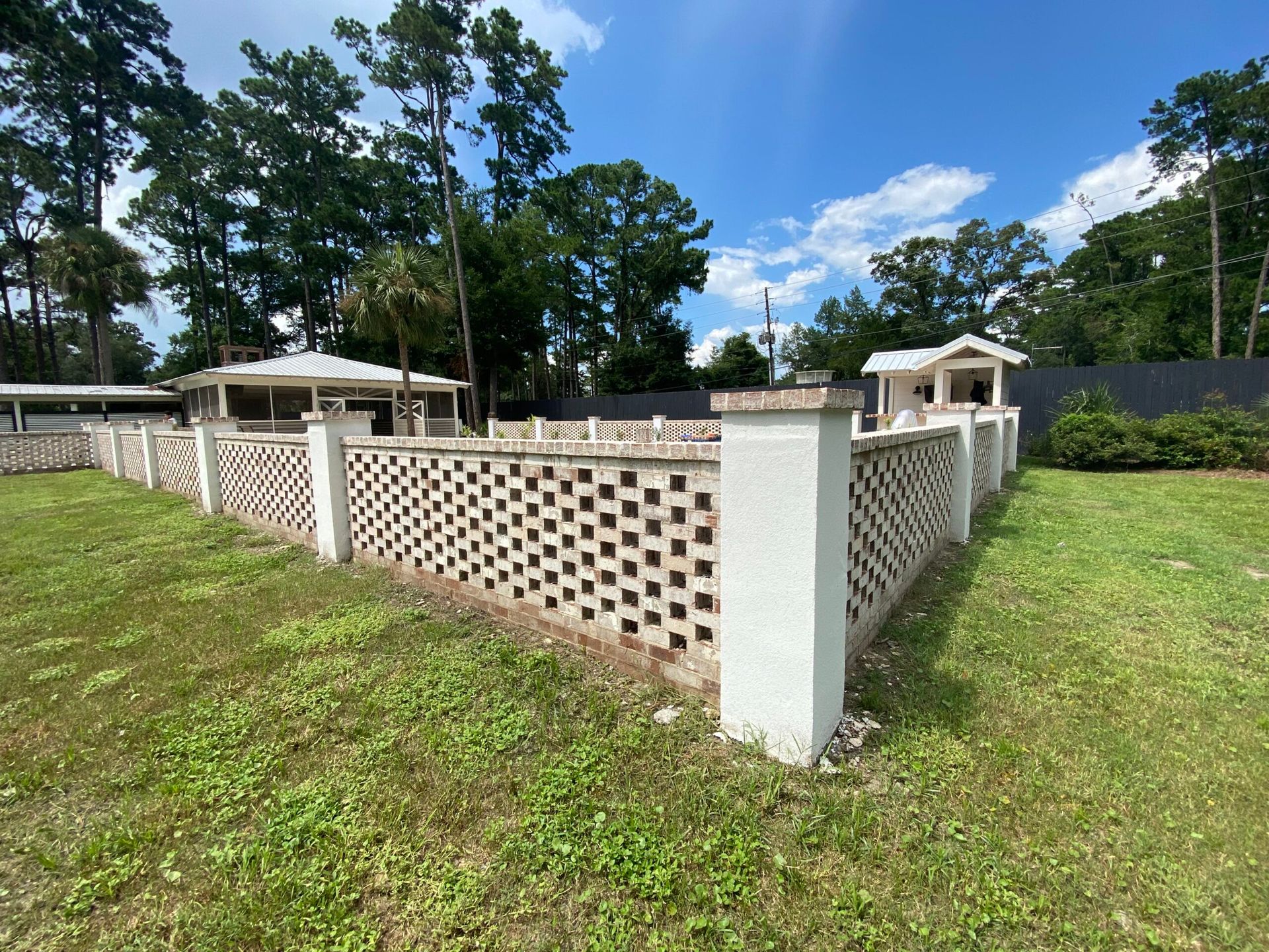 A white fence surrounds a grassy field with trees in the background