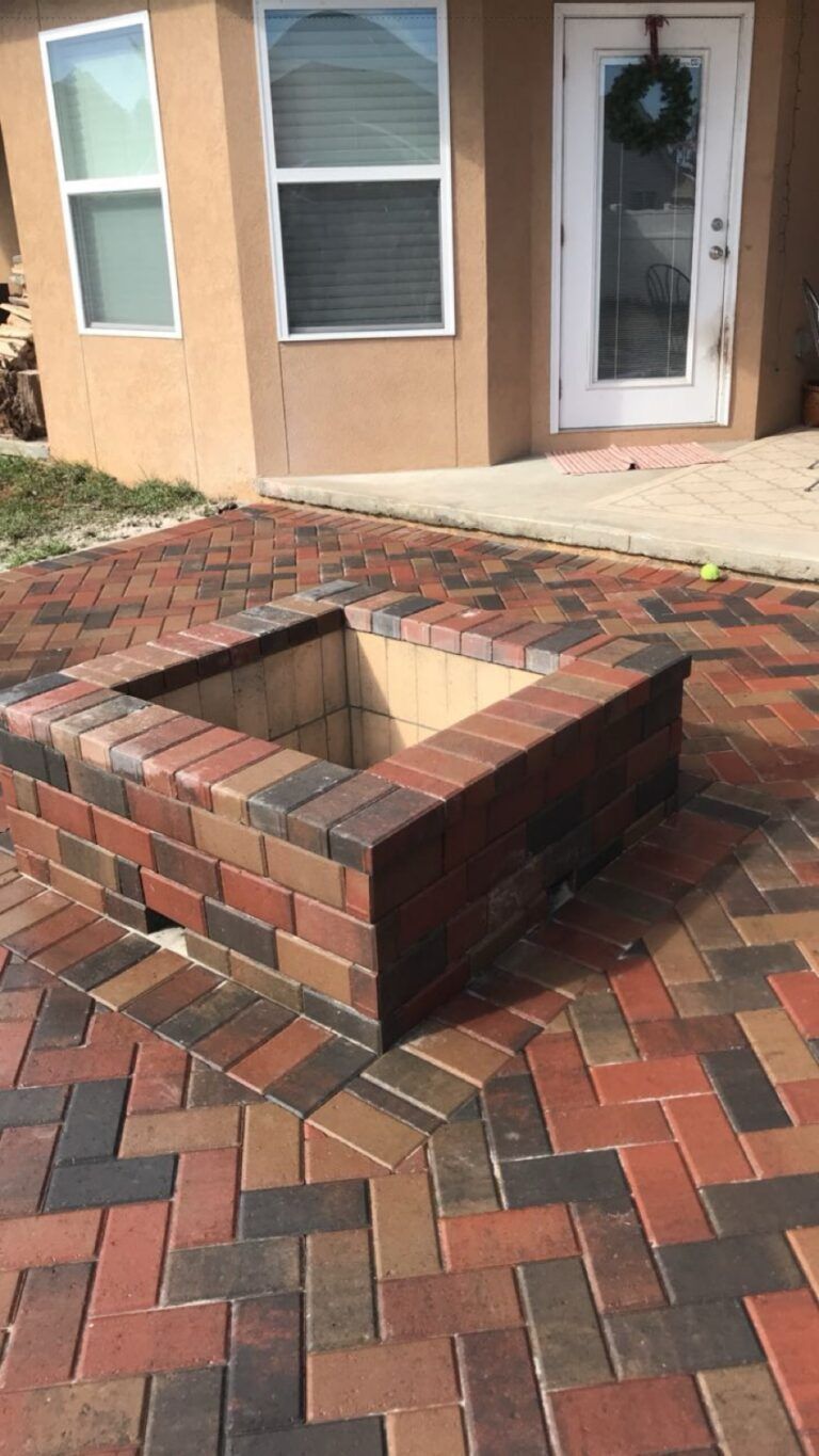 A fire pit is sitting on a brick patio in front of a house.